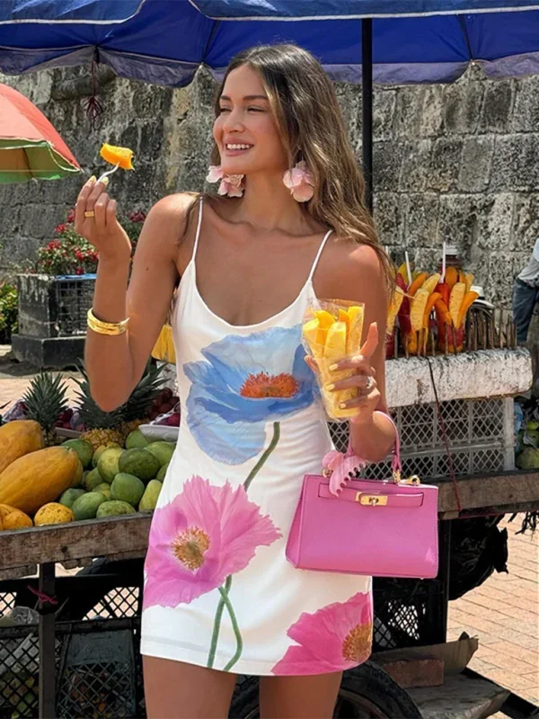 White - Woman wearing a white slip mini dress featuring a large-scale pink and blue painted floral print, styled with delicate spaghetti straps and a straight neckline.