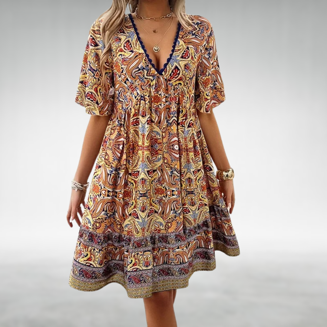 Yellow - A woman wearing a bohemian-style mini dress featuring a warm-toned paisley print, a deep V-neckline with blue crochet trim, short flutter sleeves, and a tiered hem.