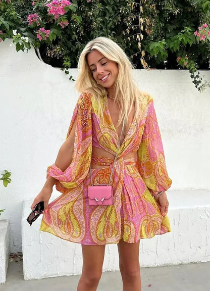 Yellow - Woman wearing a bright pink and yellow paisley print mini dress with long split sleeves, a deep V-neck, and waist cutouts.
