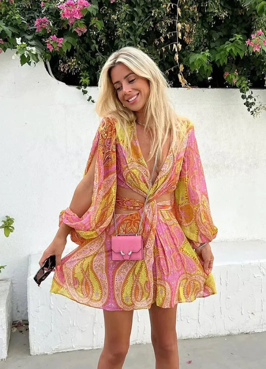 Yellow - Woman wearing a bright pink and yellow paisley print mini dress with long split sleeves, a deep V-neck, and waist cutouts.