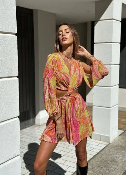 Yellow - Woman wearing a bright pink and yellow paisley print mini dress with long split sleeves, a deep V-neck, and waist cutouts.