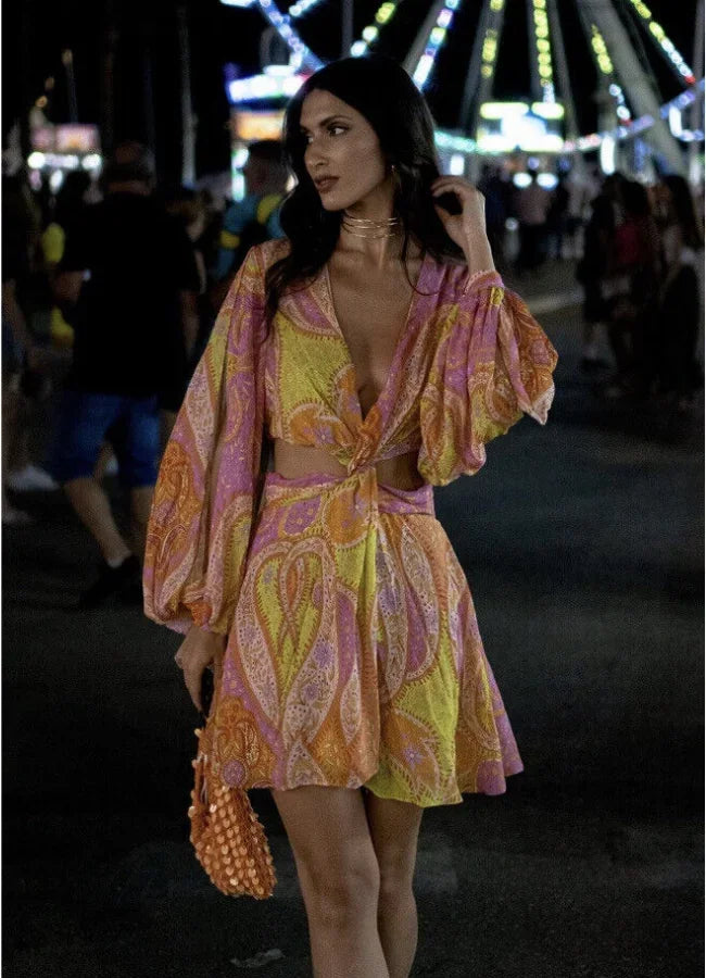 Yellow - Woman wearing a bright pink and yellow paisley print mini dress with long split sleeves, a deep V-neck, and waist cutouts.
