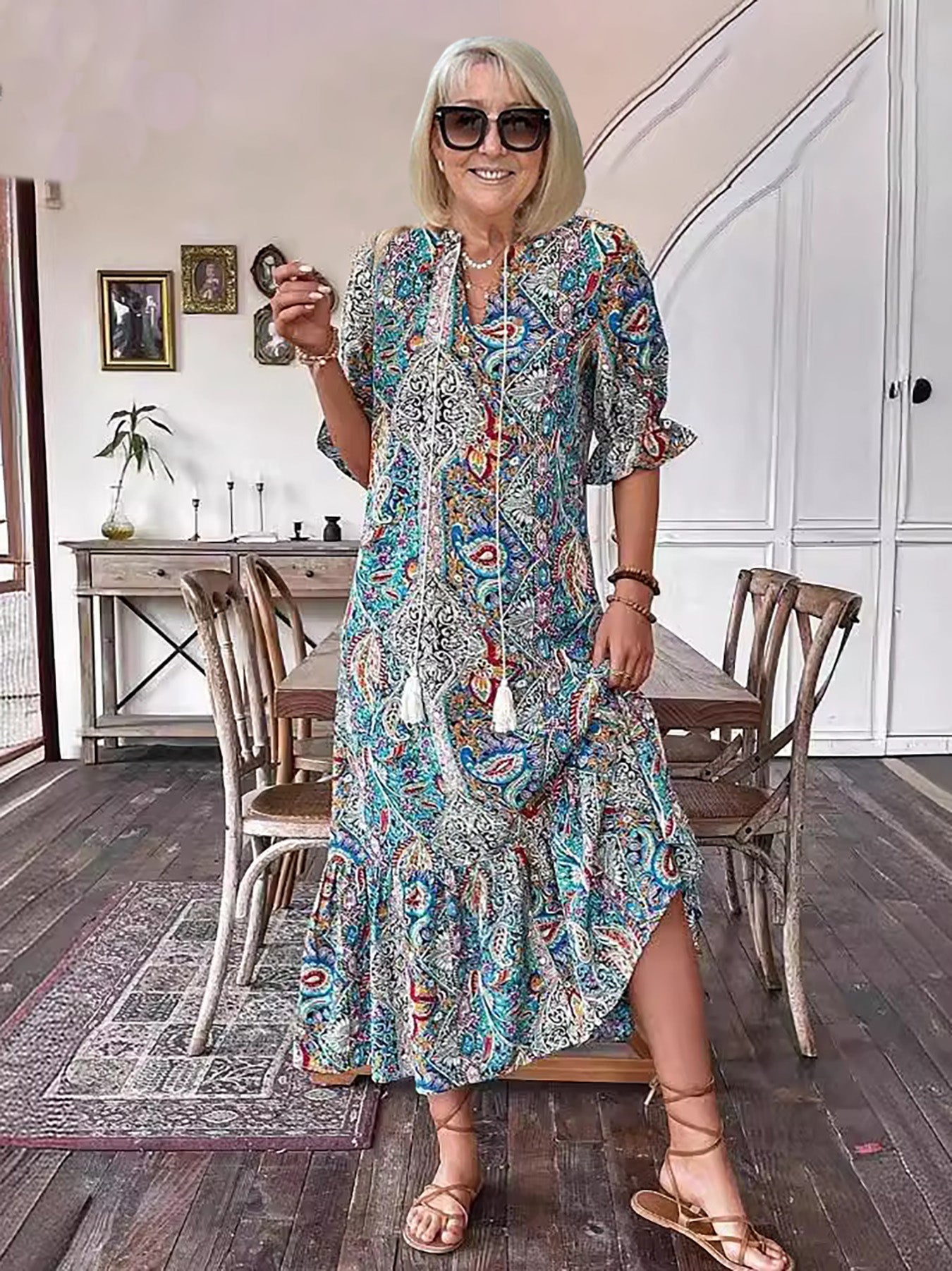 Red - A woman wearing a colorful paisley print maxi dress with a V-neckline, tassel ties, and short sleeves, holding a woven straw tote bag.
