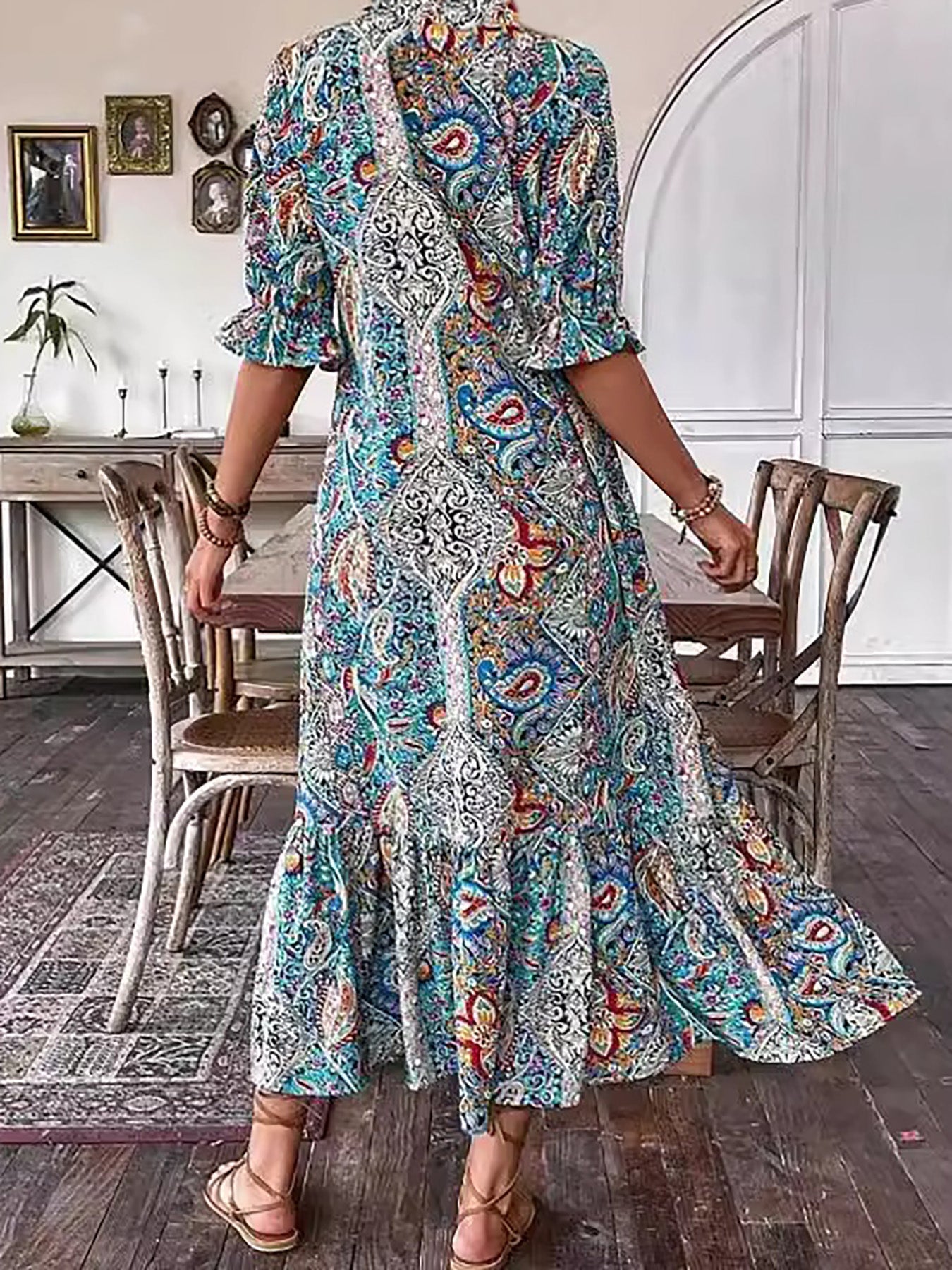 Red - A woman wearing a colorful paisley print maxi dress with a V-neckline, tassel ties, and short sleeves, holding a woven straw tote bag.