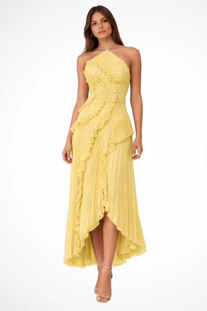 Yellow - A woman wearing a sleeveless, light pink halter maxi dress made of pleated chiffon, featuring a cascading ruffle down the front and an asymmetrical high-low hemline.