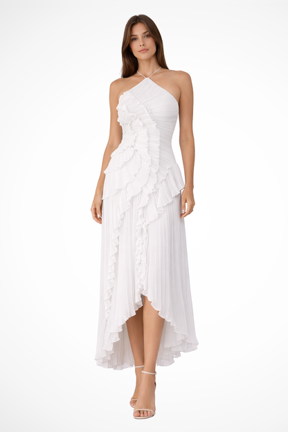 White - A woman wearing a sleeveless, light pink halter maxi dress made of pleated chiffon, featuring a cascading ruffle down the front and an asymmetrical high-low hemline.