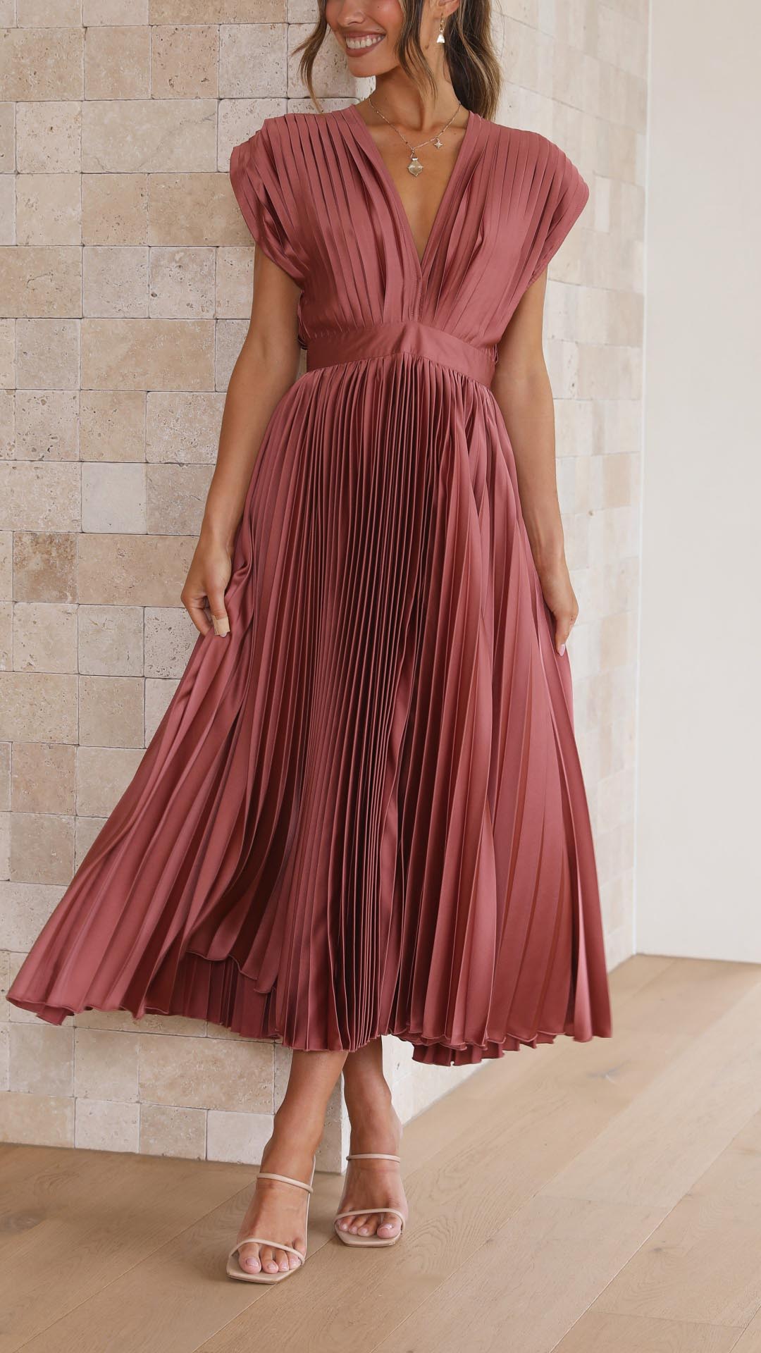 Antique Pink - Woman wearing a dusty rose pleated midi dress with a deep V-neckline and banded waist.
