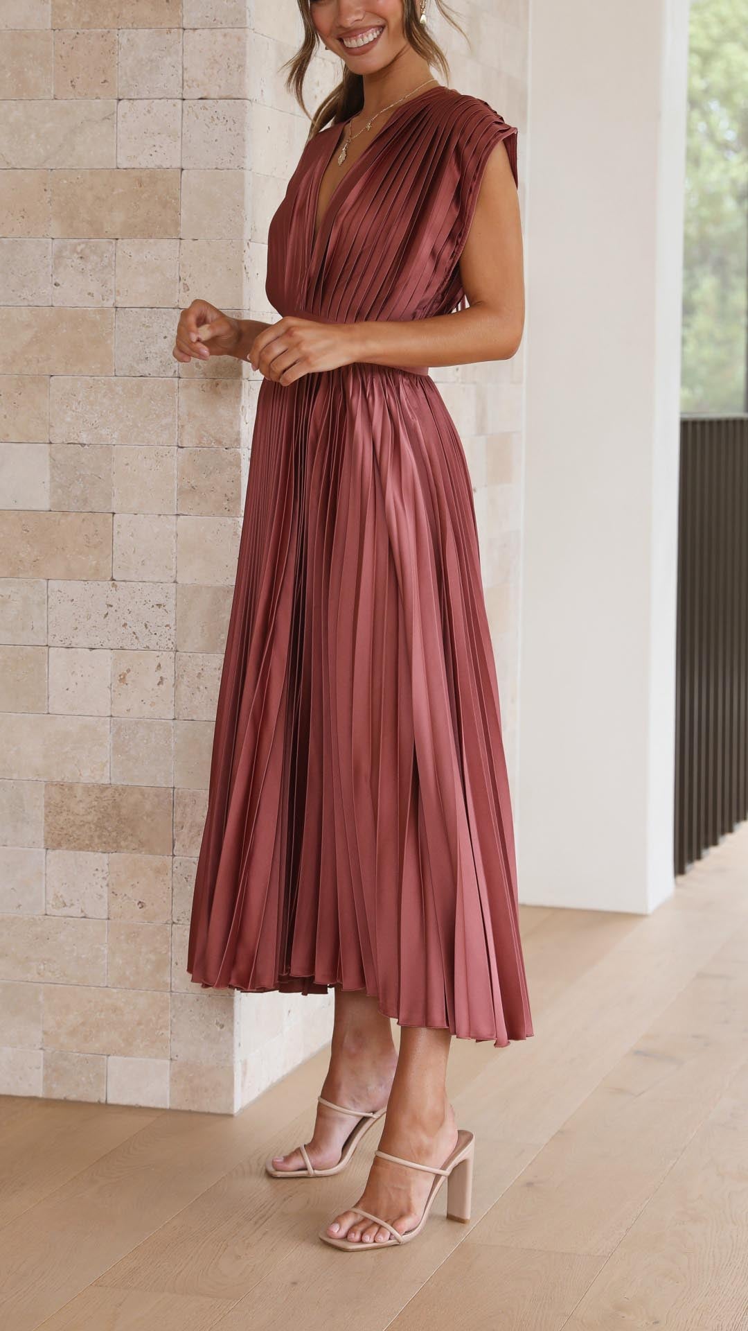 Antique Pink - Woman wearing a dusty rose pleated midi dress with a deep V-neckline and banded waist.