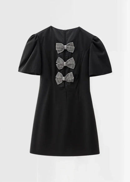 Black with pearls - Black mini dress with white polka dots, featuring short puff sleeves, a center front cutout, and three contrasting white 3D bows down the bodice.