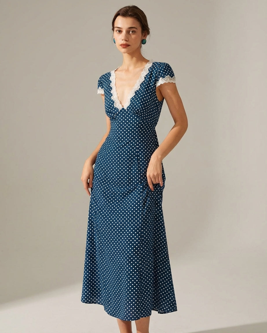 Navy - A woman wearing a navy blue and white polka dot midi dress with white lace trim along the V-neckline and cap sleeves, paired with white low-heeled slide sandals.