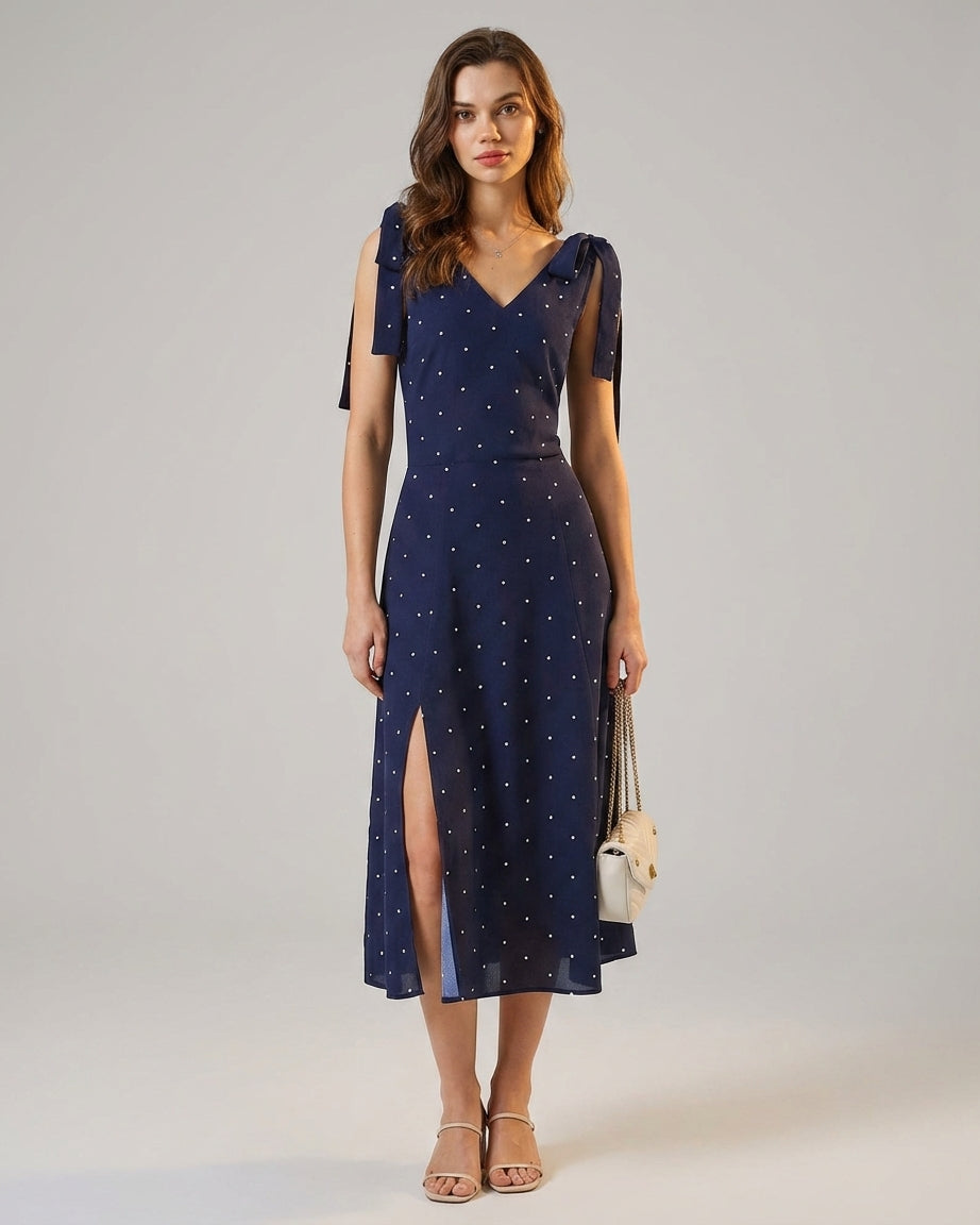 Navy - A woman wearing a navy blue and white polka dot two-piece midi set, featuring a cropped tie-shoulder V-neck top and a high-waisted midi skirt with a side slit.