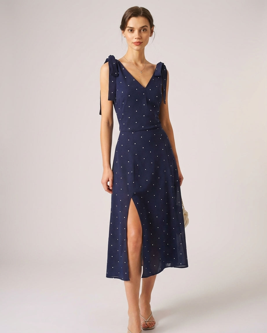 Navy - A woman wearing a navy blue and white polka dot two-piece midi set, featuring a cropped tie-shoulder V-neck top and a high-waisted midi skirt with a side slit.