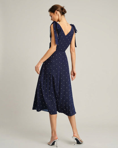Navy - A woman wearing a navy blue and white polka dot two-piece midi set, featuring a cropped tie-shoulder V-neck top and a high-waisted midi skirt with a side slit.