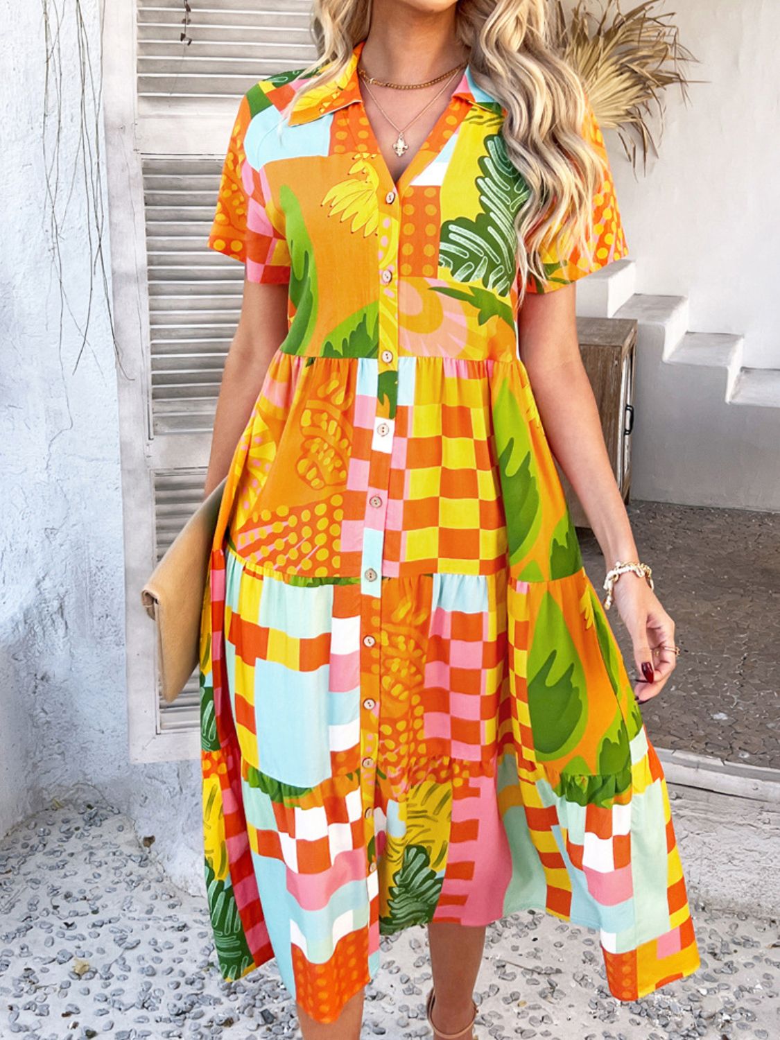 Tangerine - A woman wearing a short-sleeve, collared maxi dress with a colorful retro floral print, featuring a button-down front and a tiered skirt.