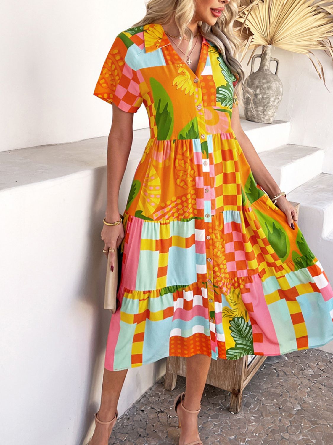 Tangerine - A woman wearing a short-sleeve, collared maxi dress with a colorful retro floral print, featuring a button-down front and a tiered skirt.