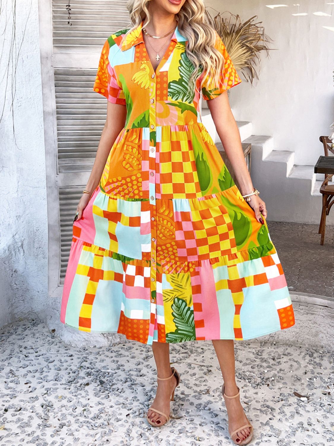 Tangerine - A woman wearing a short-sleeve, collared maxi dress with a colorful retro floral print, featuring a button-down front and a tiered skirt.