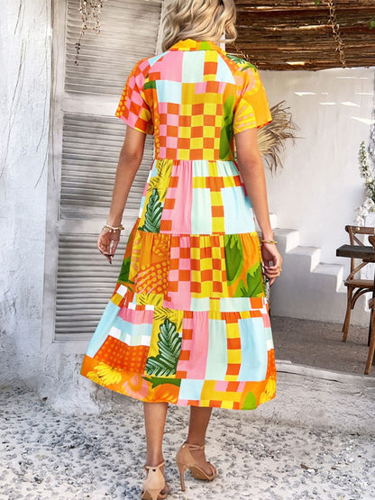 Tangerine - A woman wearing a short-sleeve, collared maxi dress with a colorful retro floral print, featuring a button-down front and a tiered skirt.