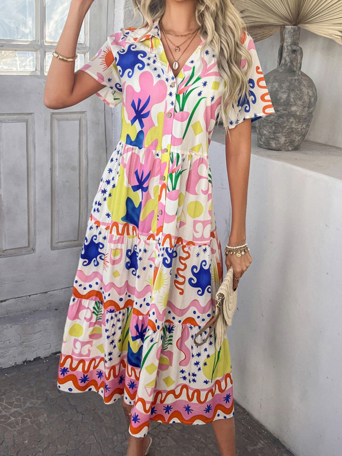 Multicolor - A woman wearing a short-sleeve, collared maxi dress with a colorful retro floral print, featuring a button-down front and a tiered skirt.