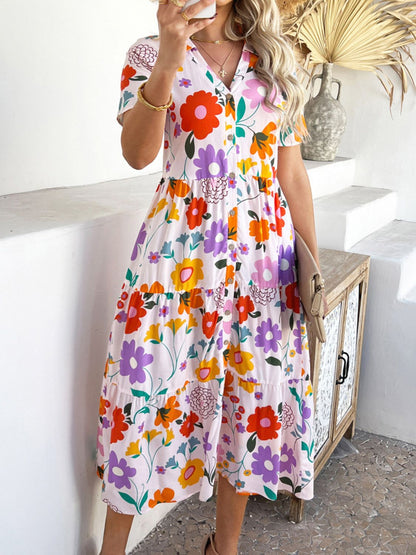Blush Pink - A woman wearing a short-sleeve, collared maxi dress with a colorful retro floral print, featuring a button-down front and a tiered skirt.