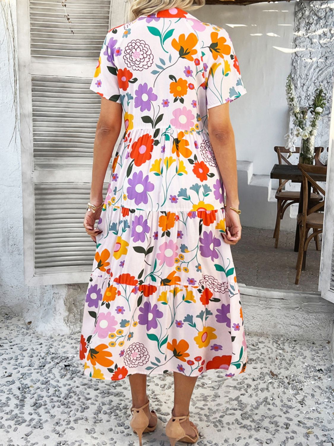 Blush Pink - A woman wearing a short-sleeve, collared maxi dress with a colorful retro floral print, featuring a button-down front and a tiered skirt.
