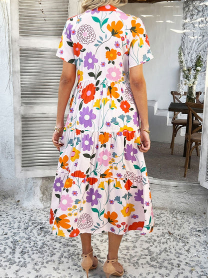 Blush Pink - A woman wearing a short-sleeve, collared maxi dress with a colorful retro floral print, featuring a button-down front and a tiered skirt.
