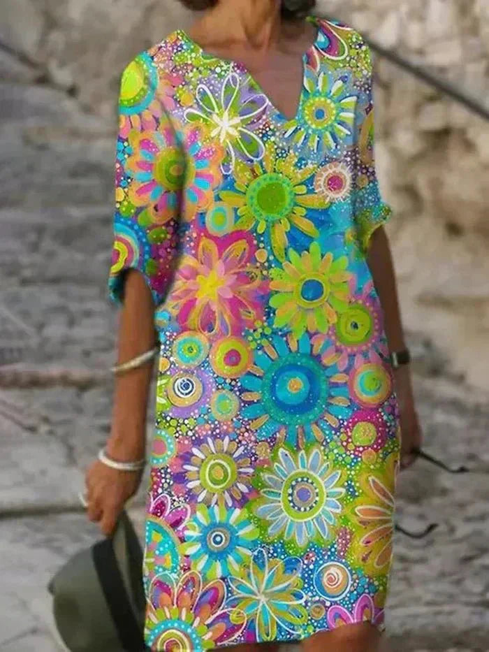 Green - A woman wearing a vibrant retro floral print shift dress with a V-neckline and short sleeves, featuring a colorful yellow, orange, and green pattern.
