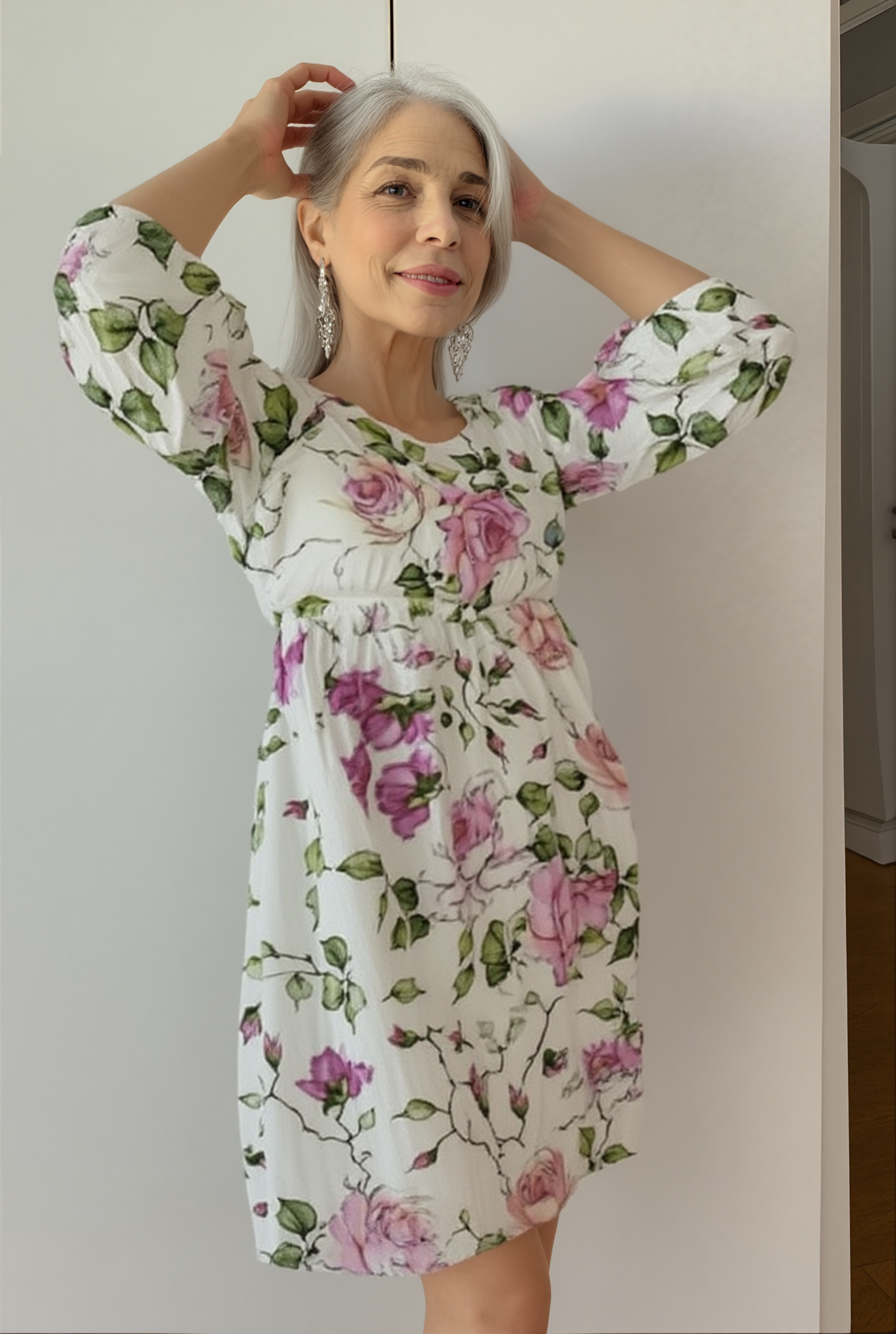 Floral - A woman on a beach wearing a white midi dress featuring a pink rose and green leaf print, three-quarter sleeves, and a relaxed linen-texture drape.