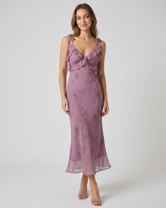 Purple - A woman wearing a dusty purple midi dress with a dark abstract floral print, featuring adjustable tie straps, a ruffled V-neckline, and a sheer chiffon hem.