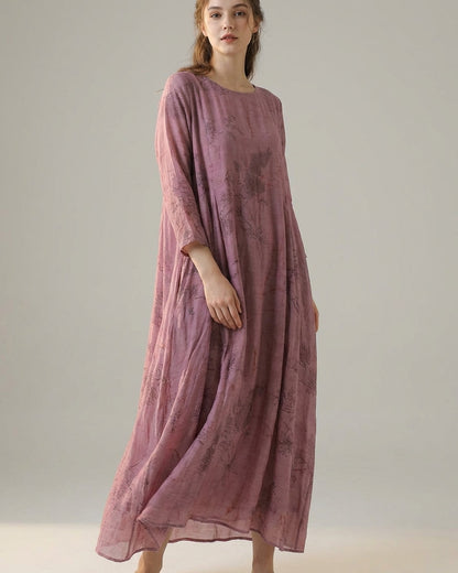 Purple - A woman wearing a dusty purple midi dress with a dark abstract floral print, featuring adjustable tie straps, a ruffled V-neckline, and a sheer chiffon hem.