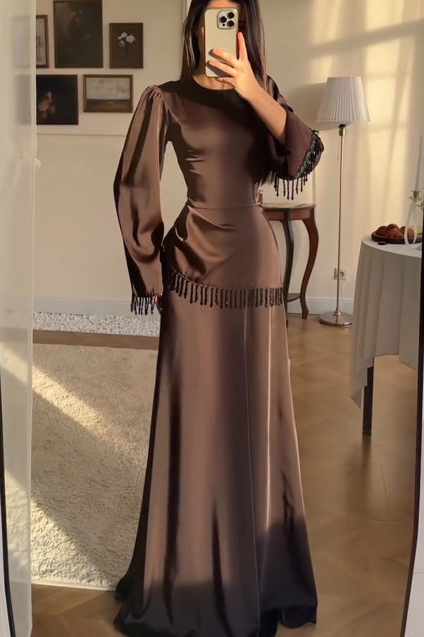 Brown - Woman wearing a chocolate brown satin long sleeve maxi dress with beaded fringe detailing at the cuffs and waistline.