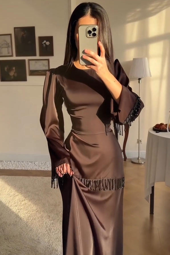 Brown - Woman wearing a chocolate brown satin long sleeve maxi dress with beaded fringe detailing at the cuffs and waistline.