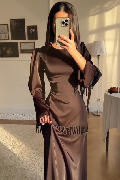 Brown - Woman wearing a chocolate brown satin long sleeve maxi dress with beaded fringe detailing at the cuffs and waistline.