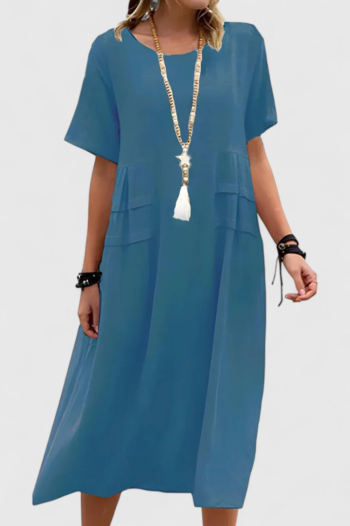 Blue - Woman wearing a light-colored, short-sleeve midi dress with front patch pockets and a relaxed A-line silhouette.