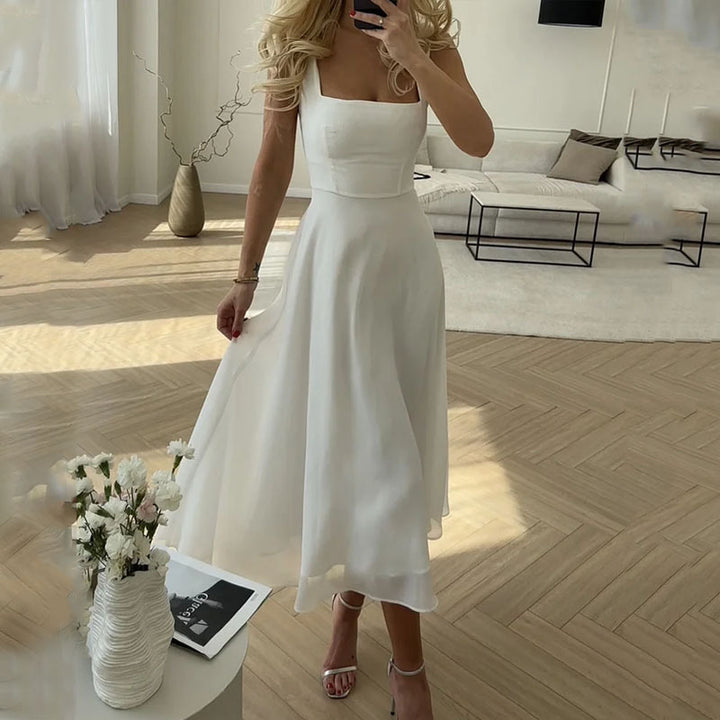 White - A woman wearing a white square-neck midi dress with a structured bodice and a flowing, double-layered chiffon A-line skirt, standing in a brightly lit minimalist room.