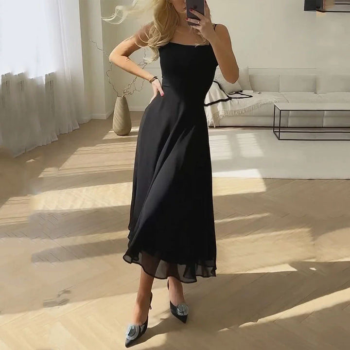 Black - A woman wearing a white square-neck midi dress with a structured bodice and a flowing, double-layered chiffon A-line skirt, standing in a brightly lit minimalist room.