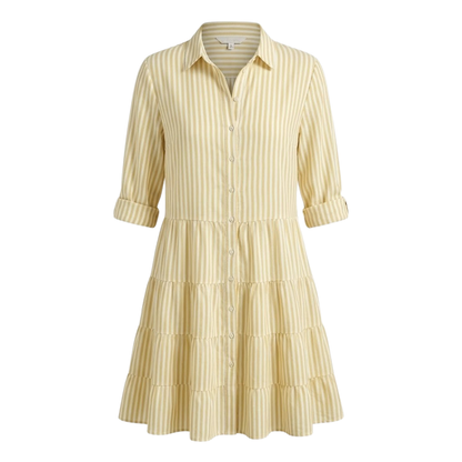 Green - A woman wearing a yellow and white vertical striped shirt dress with a collared neckline, button-down front, three-quarter sleeves, and a tiered skirt, standing on a sunlit cobblestone street.