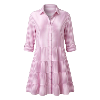 Green - A woman wearing a yellow and white vertical striped shirt dress with a collared neckline, button-down front, three-quarter sleeves, and a tiered skirt, standing on a sunlit cobblestone street.