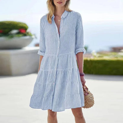 Blue - Woman wearing a green and white striped button-front tiered shirt dress with rolled sleeves and a collared neckline, carrying a woven straw bag.