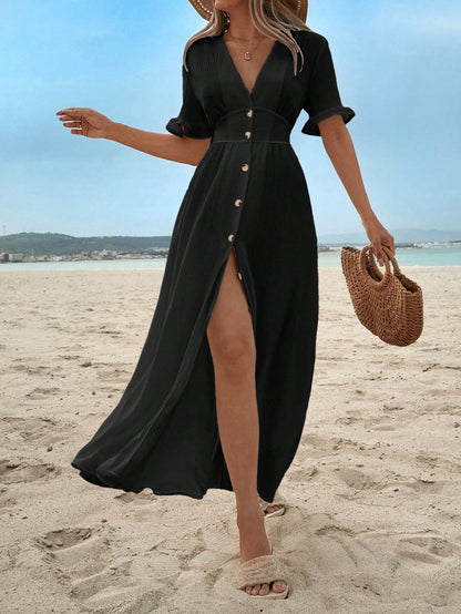 Black - A woman on a sandy beach wearing a white textured crepe maxi dress with a V-neckline, flutter sleeves, button-down front, and a high leg slit, holding a woven straw handbag.