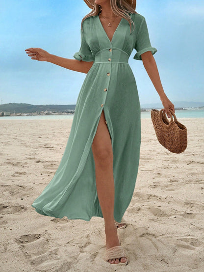 Mint Green - A woman on a sandy beach wearing a white textured crepe maxi dress with a V-neckline, flutter sleeves, button-down front, and a high leg slit, holding a woven straw handbag.