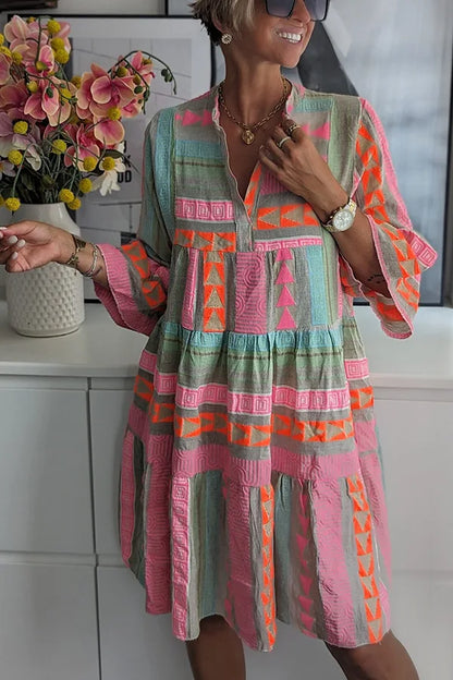 Light Green - A woman wearing a colorful, textured geometric print mini dress featuring a split neckline, three-quarter bell sleeves, and a tiered skirt.