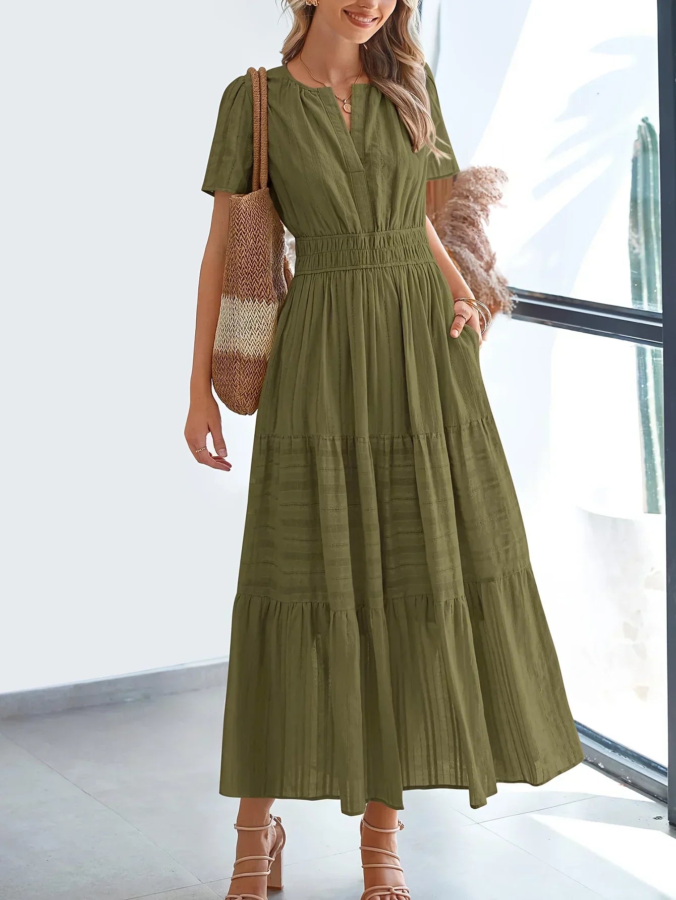 Green - A woman wearing a dusty pink, textured stripe maxi dress featuring a smocked waist, tiered skirt, short sleeves, and a split neckline, styled with a woven straw shoulder bag.