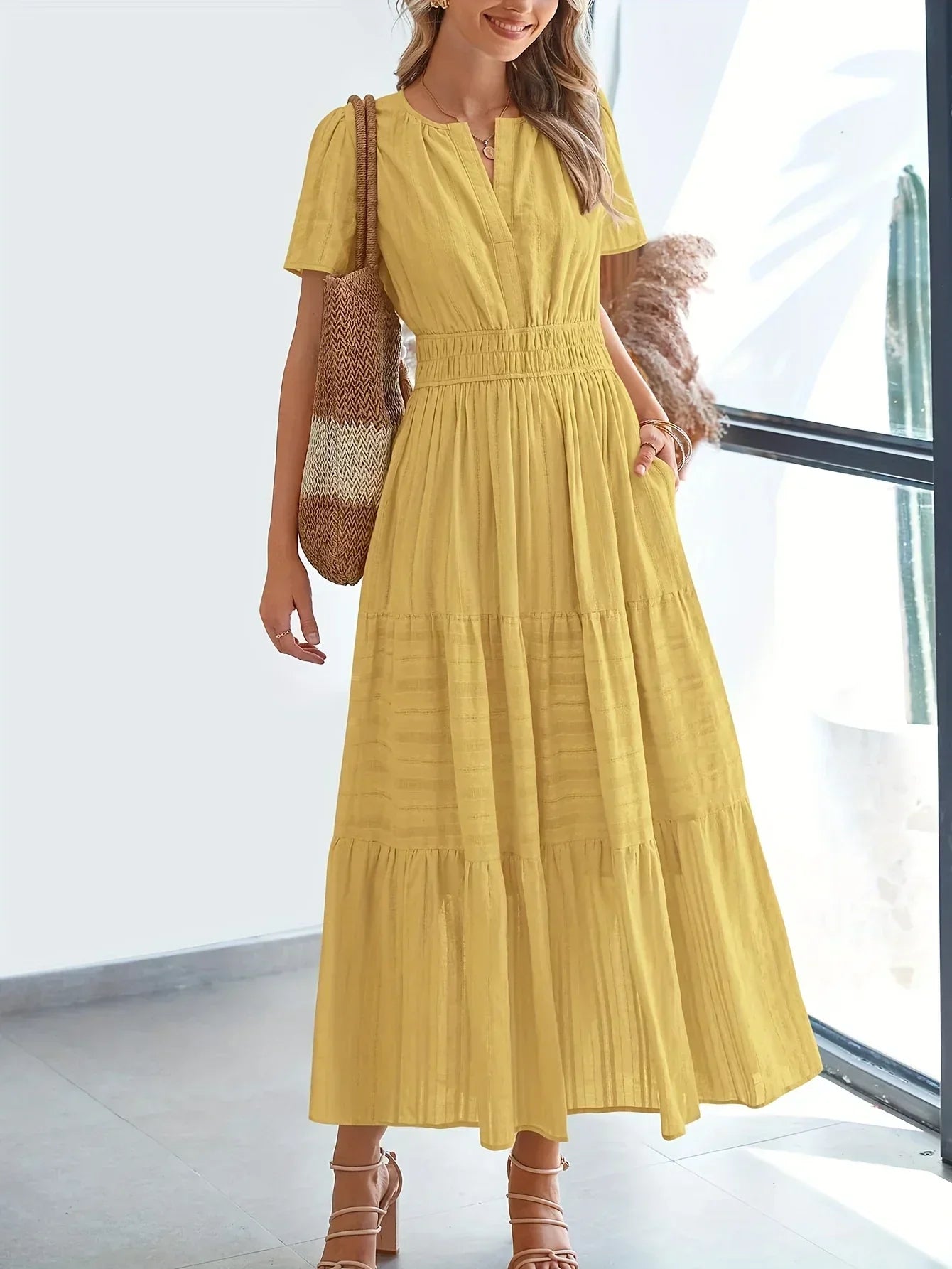 Yellow - A woman wearing a dusty pink, textured stripe maxi dress featuring a smocked waist, tiered skirt, short sleeves, and a split neckline, styled with a woven straw shoulder bag.