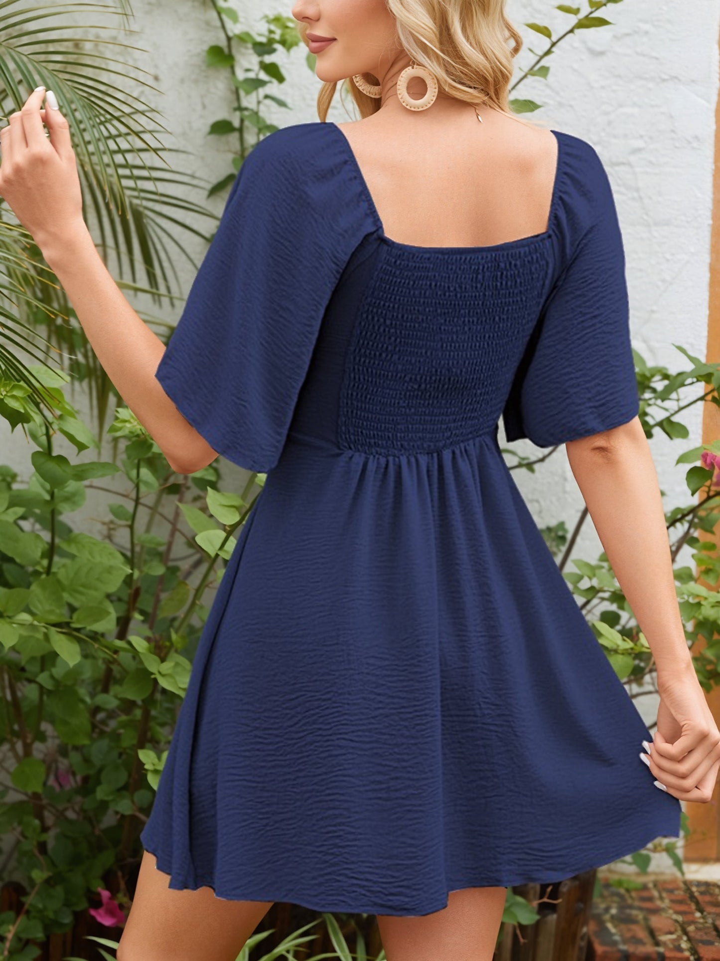 Navy Blue - Woman wearing a textured crepe mini dress with flutter sleeves and a tie front detail at the bust, accessorized with a straw hat and woven crossbody bag