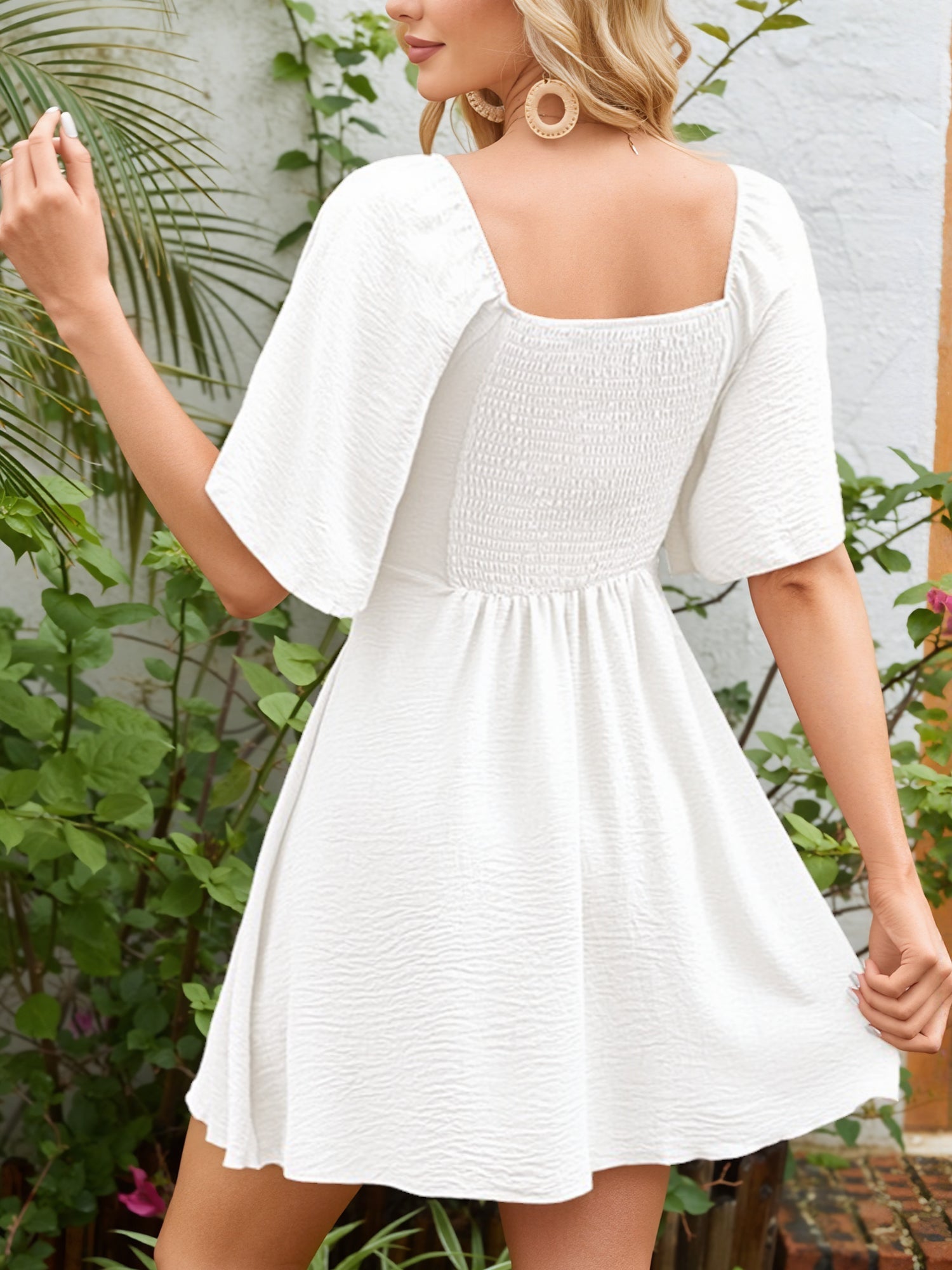 White - Woman wearing a textured crepe mini dress with flutter sleeves and a tie front detail at the bust, accessorized with a straw hat and woven crossbody bag