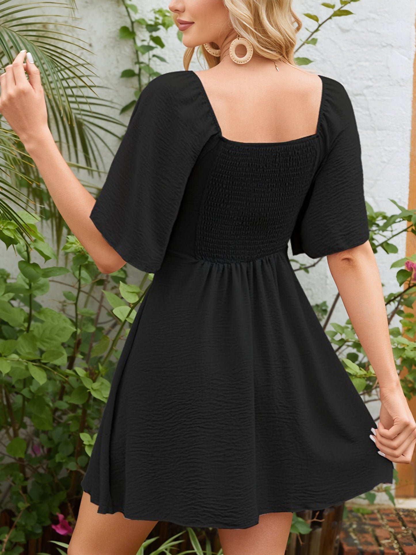 Black - Woman wearing a textured crepe mini dress with flutter sleeves and a tie front detail at the bust, accessorized with a straw hat and woven crossbody bag