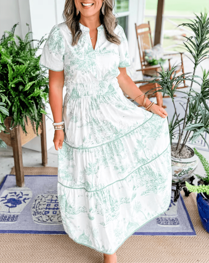 Green - A woman wearing a white and brown toile print cotton poplin maxi dress with puff sleeves, a smocked waist, and a tiered skirt.