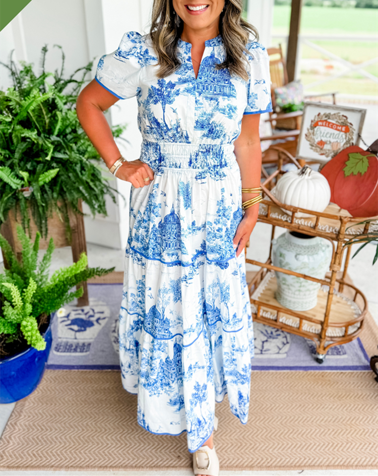 Blue - A woman wearing a white tiered maxi dress with a brown toile de Jouy print, featuring short puff sleeves, a smocked waist, and a split neckline.