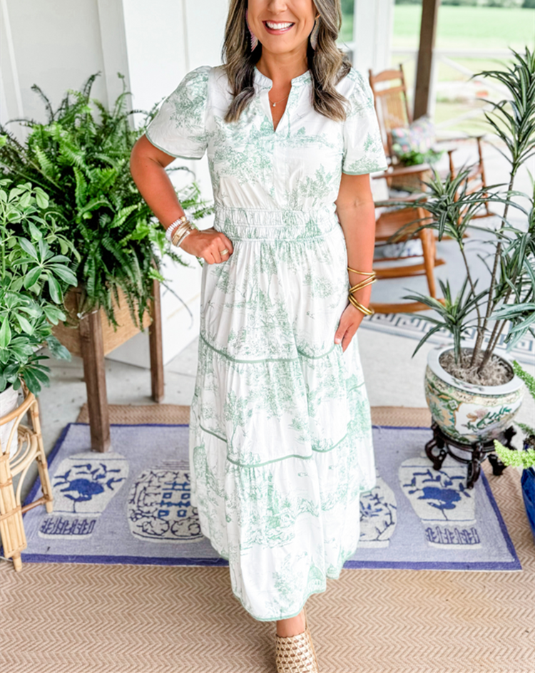 Blue - A woman wearing a white tiered maxi dress with a brown toile de Jouy print, featuring short puff sleeves, a smocked waist, and a split neckline.