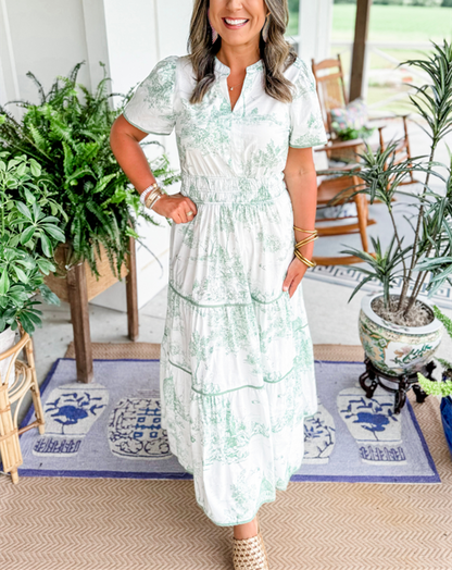 Blue - A woman wearing a white tiered maxi dress with a brown toile de Jouy print, featuring short puff sleeves, a smocked waist, and a split neckline.